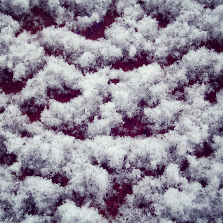 Red wooden surface covered with snow. Fluffy snowflakes on the roof. Natural background. Cold winter day. Close up. Winter in Russia. Toned photo.の写真素材