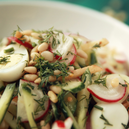 Quail eggs salad in the white bowl. Healthy lunch. European cuisine. Close up. Radish, cucumber, quail eggs and pine nuts. Ovo vegetarian dish. Toned photo.の写真素材