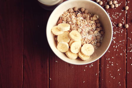 Healthy breakfast. Copy space. Granola bowl with banana, raisins and nuts and on the wooden background. Close up photo. Top view. Sweet vegan dish. Morning oatmeal closeup.の写真素材