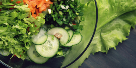 Glass bowl with cutted vegetables for a salad. Close up. Bell pepper, onion, leafy greens and cucumbers cutted in pieces. Wooden background.の写真素材