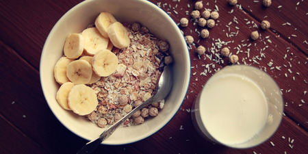 Healthy breakfast. Granola bowl with banana, raisins and nuts. And a glass of milk on the wooden background. Top view. Close up photo. Sweet vegan dish. Morning oatmeal closeup.の写真素材
