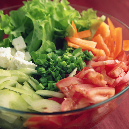 Glass bowl with cutted vegetables for a salad. Tomatoes, celery, bell pepper, onion, leafy greens and cottage cheese cutted in pieces. Lacto vegetarian dish. Close up.の写真素材