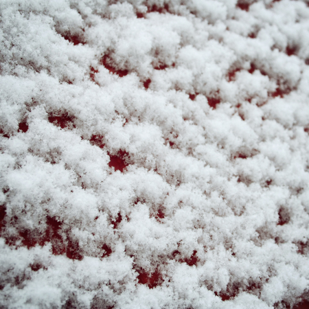 Red wooden surface covered with snow. Fluffy snowflakes on the roof. Natural background. Cold winter day. Close up. Winter in Russia. Toned photo.の写真素材