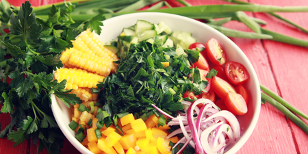 White plate with cut vegetables for a vegan salad on the red wooden table. Colorful photo. Corn, cherry tomatoes, bell pepper, onion, cucumber and garden herbs. Wide photo.の写真素材