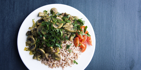 Red rice with mushrooms and cherry tomatoes. Vegan dish. European cuisine. Simple healthy lunch on the black background. Vegetarian rice dish on the white plate. Close up. Wide photo. Top view.の写真素材