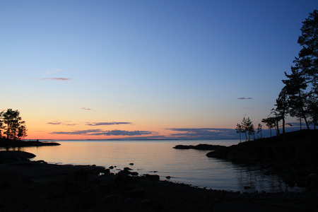 Beautiful northern landscape. Russian North. Ladoga lake at sunset. Wild nature. Trees reflected in the water. Aged photo in retro style. Summertime. Twilight. Island of Valaam, Karelia, Russia.の写真素材