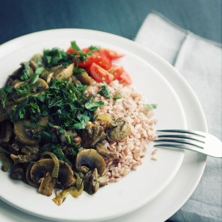 Red rice with mushrooms and cherry tomatoes. Vegan dish. European cuisine. Simple healthy lunch. Vegetarian rice dish on the white plate. Close up. Toned photo.の写真素材