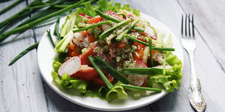 Spring Vegetable Salad on the white plate. Radish, tomato, celery and cucumber. Topped with sesame seeds. Vegetarian dish on the white wooden table. Close up. Wide photo.の写真素材