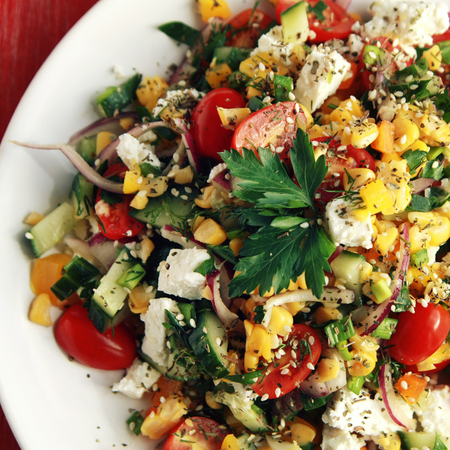 Colorful vegetable mix. Simple low calories salad. Cherry tomatoes, sweet corn, cucumber, bell pepper and cottage cheese. Weight loss dish. European cuisine. Top view. Toned photo.の写真素材