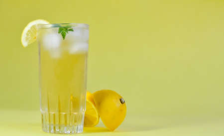 Highball glass with iced tea decorated with lemon and mint on a yellow background