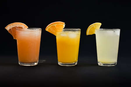 Three glasses of freshly squeezed orange juice, grapefruit juice, and lemon juice lined up on a black backgroundの写真素材