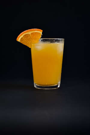 Photo of a glass of cold orange juice with a piece of orange as a decoration on a black backgroundの写真素材