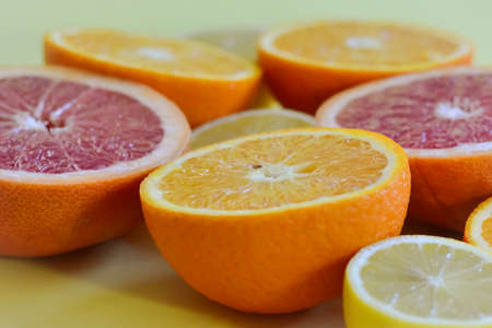 Photo of oranges and citruses cut in half on a yellow backgroundの写真素材