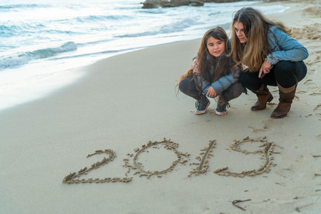 Mother and daughter looking at 2019 written on the sandの写真素材