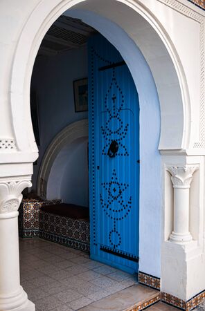 A large entrance of a typical tunisian white house with the traditiona blue door with ornaments