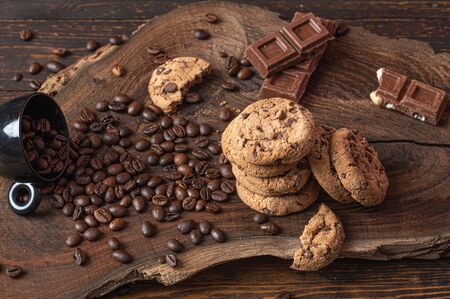 Piled up cookies, pieces of chocolate and coffe beans over a wooden boardの写真素材