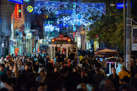A crowded street at night time with the historic red tram passing in the middle of the crowd in Istanbul, Turkeyのeditorial素材
