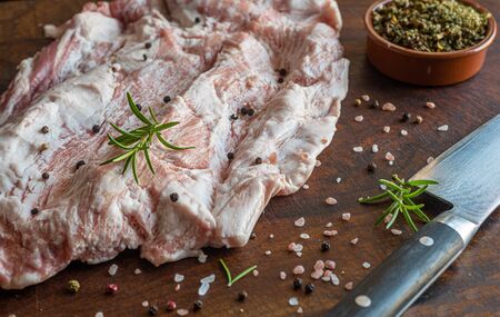 Close up of raw pork Secreto de ventresca pure iberico, iberian pig cut, with himalayan pink salt, pepper in grains, rosemary and a knife on a wooden boardの写真素材
