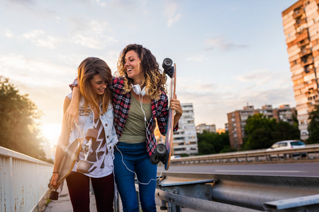 Smiling skate girls holding long-boards walking outdoors in the street having funの写真素材