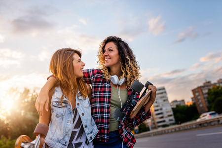 Smiling skate girls holding long-boards walking outdoors in the street having funの写真素材