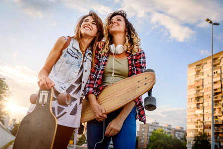 Beautiful smiling young woman skater with a long board standing in the streetの写真素材