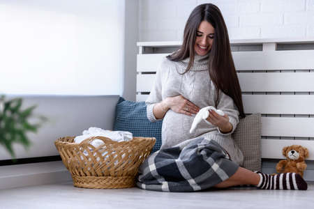 Beautiful young smiling pregnant woman preparing clothes for her baby.