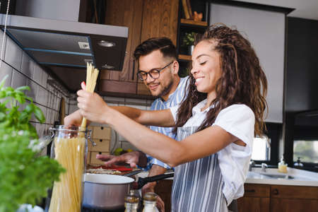 Young cheerful multi-ethnic couple preparing pasta together at their modern kitchenの写真素材