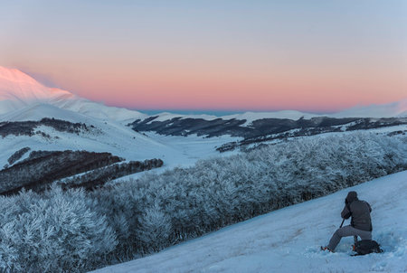 Photographer working in the mountains in winter at sunset with snow, Sibillini mountains NP, Umbria, Italyの写真素材