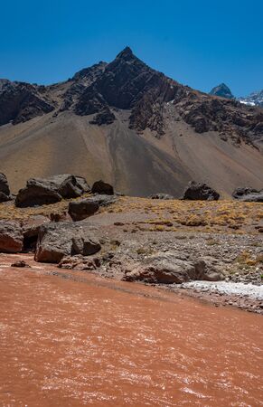 Beautiful vertical landscape with rocky mountains and reddish stream in Las Cuevas, Mendoza, Argentina. Las cuevas is the last town on the border with Chileの写真素材