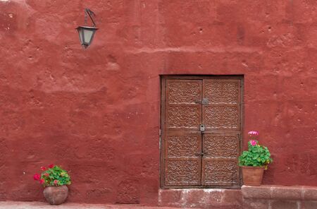 Beautiful ancient door with flower pots, lantern and red wall in Arequipa, Peruの写真素材