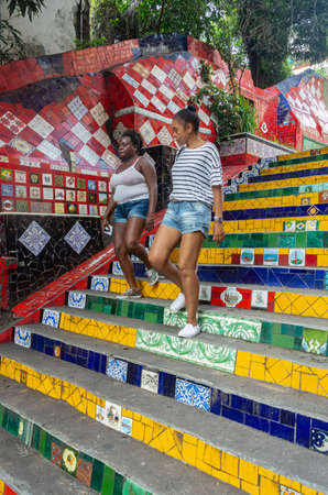 RIO DE JANEIRO, BRAZIL - JANUARY 3, 2020: Brazilian girls down the colorful steps of the famous Stairway Selaron (Escadaria Selaron). This landmark was designed by the chilean artist Jorge Selaron who declared it as "my tribute to the Brazilian people".のeditorial素材