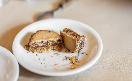 Close up of a typical homemade Argentinian alfajor filled with dulce de leche on a white plate. Argentina is the world's biggest producer and consumer of this sweet. Its inhabitants consume 6 million alfajores per day and are an integral part of Argentine popular culture. An alfajor is a pair of soft, crumbly biscuits sandwiching a layer of dulce de leche, it is like a cross between a biscuit and a cake.の写真素材
