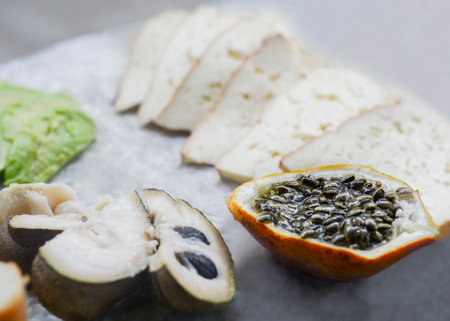 Close up of slices of healthy tropical fruit custard apple or sugar apple, also called custard apple and passion fruit also called maracuya, with slices of avocado in the backgroundの写真素材