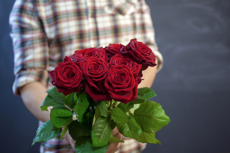 the guy in the plaid shirt holds a bouquet of red roses in his hand, focus on flowers.. background of chalk boardsの写真素材