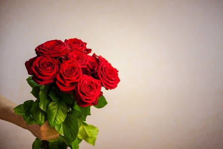 male hand holding a bouquet of red roses beige backgroundの写真素材