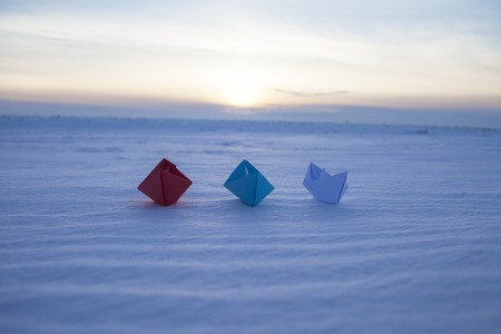 Red, blue and white paper boat in the snow. Winter