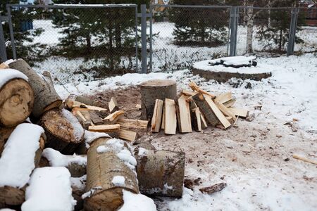 The chopped wood in the winter. A pile of wood and an axe in the stump. Stacked chopped wood for the...