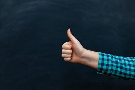 hand giving thumbs up on blackboard. Close up of thumbs up hand sign gesture of approval on chalkboard texture background. Upの写真素材