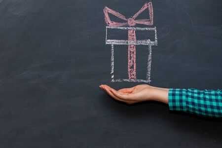 Outstretched woman's palm a holiday gift box . The chalk Board in the background.の写真素材