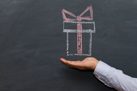 Outstretched man palm a holiday gift box . The chalk Board in the backgroundの写真素材