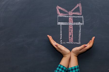 Outstretched woman's palm a holiday gift box . The chalk Board in the backgroundの写真素材