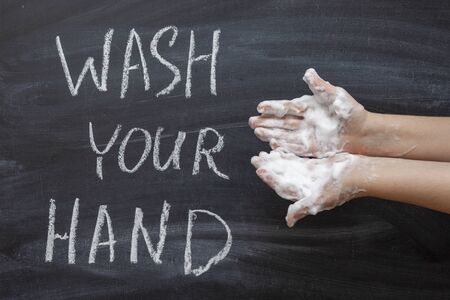 Women's hands in soap suds on the background of a chalkboard with the text "Wash Your Hands". The concept of hygieneの写真素材