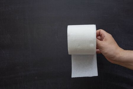 A hand holds a roll of toilet paper against a chalkboard background.の写真素材