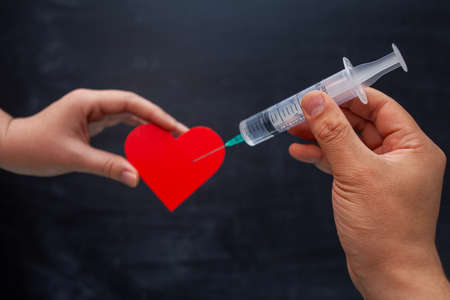 A hand with a disposable syringe makes an injection into the heart symbolの写真素材