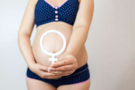 A pregnant woman holds the gender symbol of a woman. Waiting for the birth of a girlの写真素材