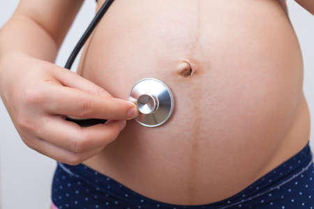 Pregnant woman with a stethoscope listens to her baby's heartbeatの写真素材