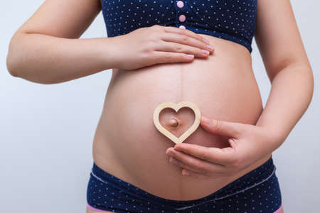 A pregnant woman holds a heart symbol against the background of her stomach
