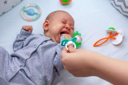mom tries to give a pacifier to a crying baby. Selective focusの写真素材
