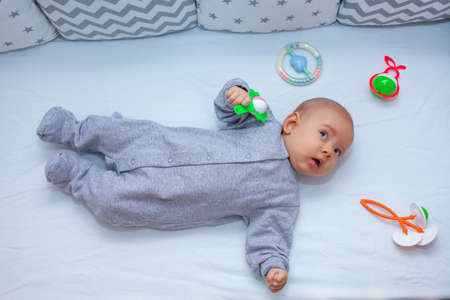 newborn baby on the bed next to lying toys rattles