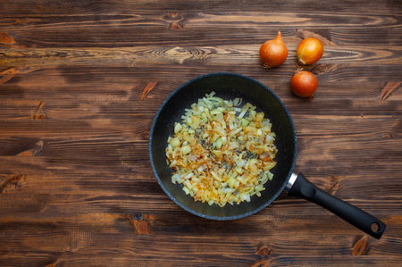 Frying pan with fried onions, three onions side by side. Brown wood background.の写真素材